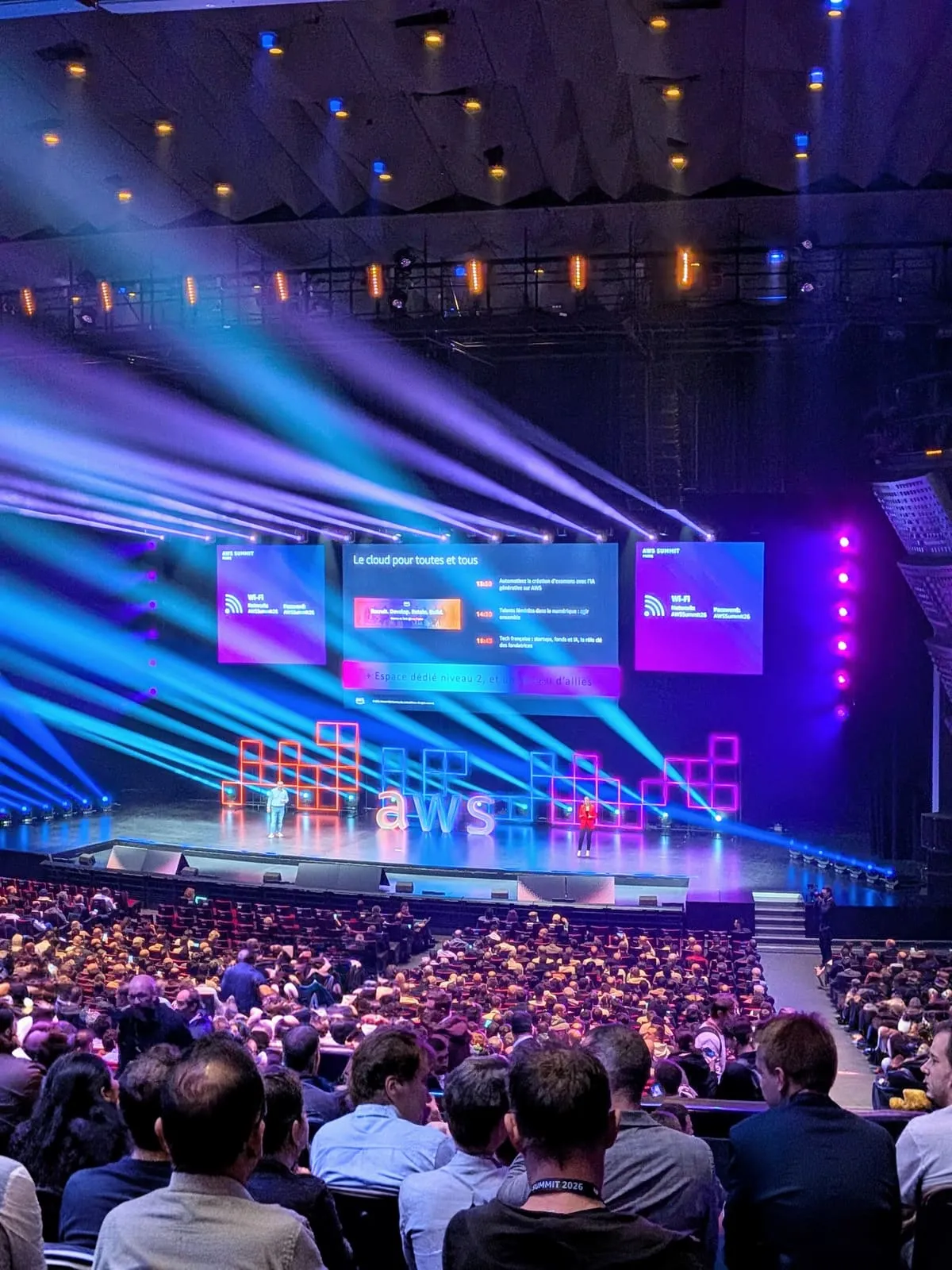 Salle plénière comble de l’AWS Summit Paris 2026 pendant la keynote, avec la scène éclairée, le logo AWS et les écrans géants « Le cloud pour toutes et tous »